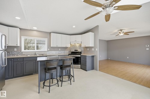 Modern kitchen featuring two-tone cabinetry with white upper and dark gray lower units, stainless steel appliances, and a central island with bar seating - 106 Springfield Crescent, Spruce Grove, AB - Indoor Photo Showing Kitchen