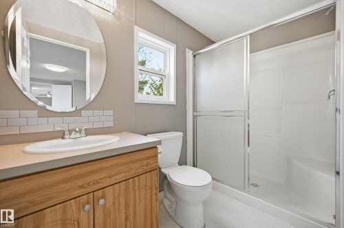 Bathroom featuring a vanity with wood-finish cabinetry and an integrated sink, subway tile backsplash, and an oval mirror - 106 Springfield Crescent, Spruce Grove, AB - Indoor Photo Showing Bathroom
