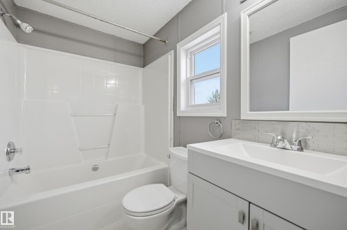 Bathroom featuring a white bathtub and shower surround, a single vanity with a rectangular sink, a white framed mirror, and a window with white trim - 106 Springfield Crescent, Spruce Grove, AB - Indoor Photo Showing Bathroom