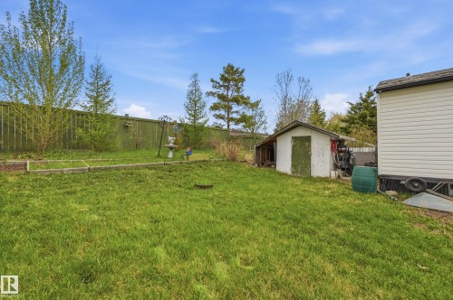 Expansive green lawn with a white storage shed featuring a green door - 106 Springfield Crescent, Spruce Grove, AB - Outdoor