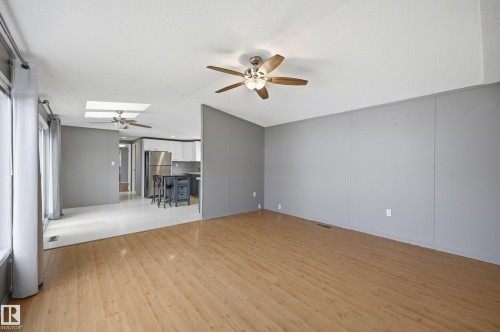 Spacious living area featuring light wood-finish flooring, a ceiling fan with light fixture, and contemporary gray wall panels - 106 Springfield Crescent, Spruce Grove, AB - Indoor Photo Showing Other Room