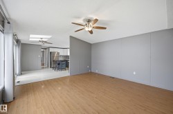Spacious living area featuring light wood-finish flooring, a ceiling fan with light fixture, and contemporary gray wall panels - 