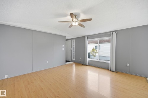 Open concept living space featuring wood-finish flooring, a ceiling fan with integrated lighting, and a large front window with white trim - 106 Springfield Crescent, Spruce Grove, AB - Indoor Photo Showing Other Room