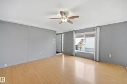 Open concept living space featuring wood-finish flooring, a ceiling fan with integrated lighting, and a large front window with white trim - 