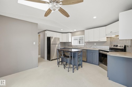 Open-concept kitchen featuring white upper cabinetry, blue lower cabinetry, stainless steel appliances, a mosaic tile backsplash, and a central island with seating - 106 Springfield Crescent, Spruce Grove, AB - Indoor Photo Showing Kitchen