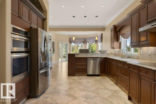 Kitchen featuring extensive wood cabinetry, stainless steel appliances including a double oven and refrigerator, granite countertops, and tile flooring - 58 Riverstone Close, Rural Sturgeon County, AB - Indoor Photo Showing Kitchen