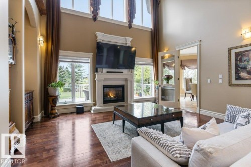 Spacious living area featuring high ceilings, rich wood-finish flooring, and a fireplace with an ornate mantel - 58 Riverstone Close, Rural Sturgeon County, AB - Indoor Photo Showing Living Room With Fireplace