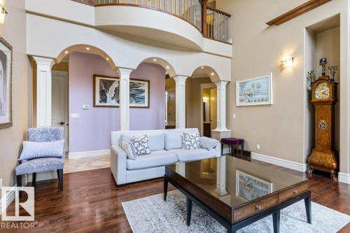 Hardwood flooring extends throughout this expansive living area, featuring architectural arches, recessed lighting, a second-story overlook, and decorative wall sconces - 58 Riverstone Close, Rural Sturgeon County, AB - Indoor Photo Showing Living Room