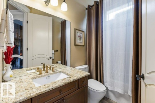 Bathroom featuring a wood-finish vanity with a light-toned, speckled countertop, an undermount sink, and a brushed bronze faucet - 58 Riverstone Close, Rural Sturgeon County, AB - Indoor Photo Showing Bathroom