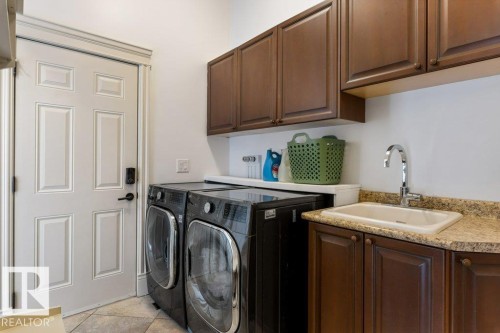 Dedicated laundry area featuring a utility sink with a chrome faucet, granite-finish countertop, and dark wood cabinetry - 58 Riverstone Close, Rural Sturgeon County, AB - Indoor Photo Showing Laundry Room
