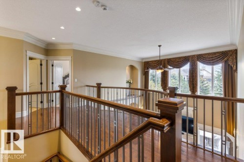 Upper-level landing featuring wood-finish flooring, dark wood railings with metal spindles, and a trio of large windows with decorative valances - 58 Riverstone Close, Rural Sturgeon County, AB - Indoor Photo Showing Other Room