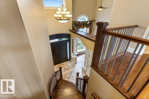 Two-story foyer featuring a grand chandelier, arched transom window, wood-finish flooring, and a curved staircase with wood and metal railings - 58 Riverstone Close, Rural Sturgeon County, AB - Indoor Photo Showing Other Room