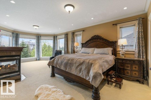 Spacious room featuring a curved wall of windows, recessed lighting, and a built-in fireplace with a stone surround - 58 Riverstone Close, Rural Sturgeon County, AB - Indoor Photo Showing Bedroom With Fireplace