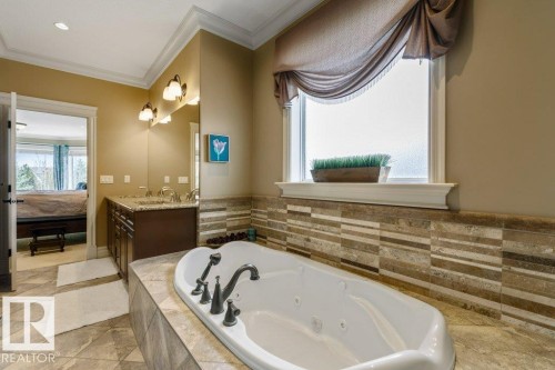 Soaking tub with bronze fixtures, dual vanity with undermount sinks, stone countertop, crown molding, and tiled flooring - 58 Riverstone Close, Rural Sturgeon County, AB - Indoor Photo Showing Bathroom