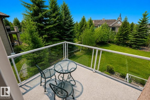 Private balcony featuring a glass railing system and durable outdoor carpeting, overlooking a sprawling green lawn and mature evergreen trees - 58 Riverstone Close, Rural Sturgeon County, AB - Outdoor