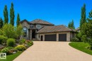 Stone and stucco exterior featuring a grand arched window, a multi-car garage, a concrete driveway, and established landscaping with mature trees and shrubs - 58 Riverstone Close, Rural Sturgeon County, AB  - Outdoor With Facade 
