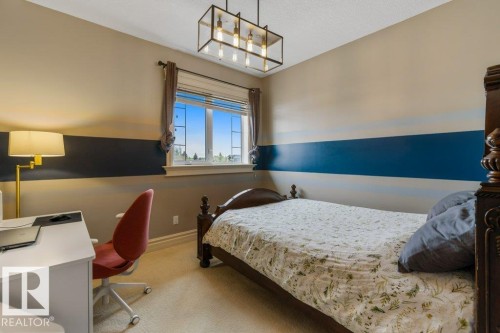 Carpeted bedroom featuring a large window, a linear chandelier, detailed baseboards, and a neutral color palette with a blue accent stripe - 58 Riverstone Close, Rural Sturgeon County, AB - Indoor Photo Showing Bedroom
