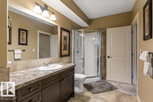Full bathroom featuring a dark wood vanity with ample storage, a spacious countertop, a ceramic sink, a mirror with overhead lighting, and a glass-enclosed shower - 58 Riverstone Close, Rural Sturgeon County, AB - Indoor Photo Showing Bathroom