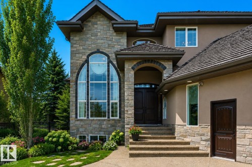 Stone and stucco exterior featuring an arched entrance, multi-pane arched window, dark wood double entry doors, textured roof, and landscaped garden beds - 58 Riverstone Close, Rural Sturgeon County, AB - Outdoor With Facade