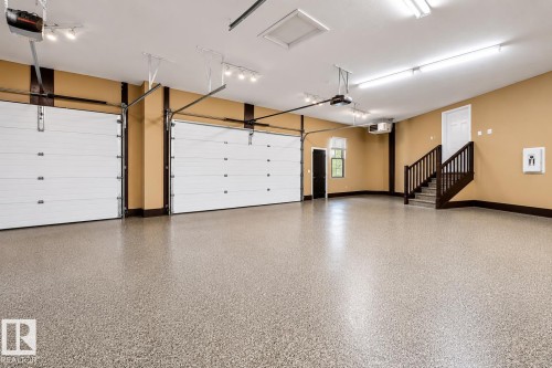 Spacious garage with a speckled epoxy floor, two overhead garage doors, a built-in staircase with wood railing, recessed lighting, and a white interior door - 58 Riverstone Close, Rural Sturgeon County, AB - Indoor Photo Showing Garage
