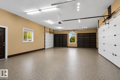 Spacious garage featuring a speckled epoxy floor, multiple windows for natural light, extensive built-in shelving, and two large overhead doors - 58 Riverstone Close, Rural Sturgeon County, AB - Indoor Photo Showing Garage