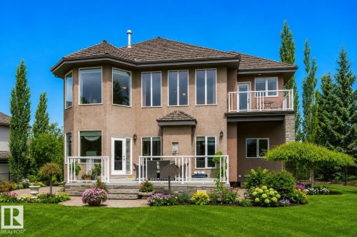 Stucco exterior with a multi-level deck and balcony, set against a vibrant green lawn - 58 Riverstone Close, Rural Sturgeon County, AB - Outdoor With Facade