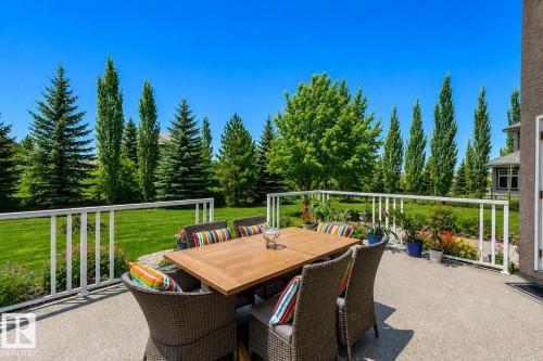 Spacious outdoor patio featuring a textured concrete surface, white railing, and a large grassy yard bordered by mature trees - 58 Riverstone Close, Rural Sturgeon County, AB - Outdoor