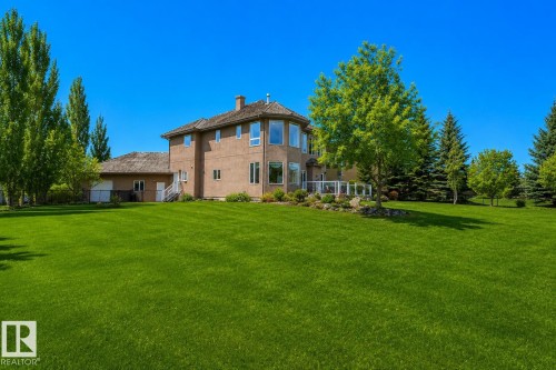 Two-story stucco property featuring a multi-level deck with glass railing, a secondary attached structure, mature trees, and a spacious lawn - 58 Riverstone Close, Rural Sturgeon County, AB - Outdoor