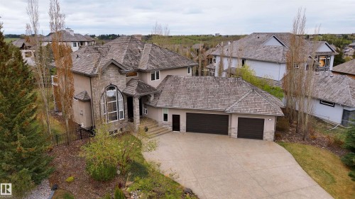 Stucco and stone exterior featuring a prominent arched window, multi-gabled roofline with cedar shakes, a multi-car garage, and a concrete driveway - 58 Riverstone Close, Rural Sturgeon County, AB - Outdoor With Facade