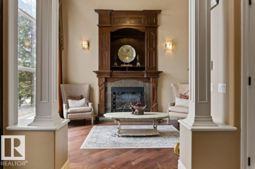 Formal living area featuring wood-finish flooring with a herringbone pattern, a built-in wood mantel with integrated shelving, a stone-surround fireplace, and decorative wall sconces - 58 Riverstone Close, Rural Sturgeon County, AB - Indoor Photo Showing Living Room With Fireplace