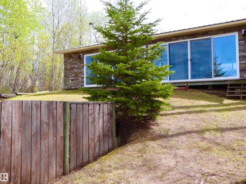 Stone veneer exterior with a prominent evergreen tree and a wooden fence - #26 5508 Twp Rd 593A, Rural Barrhead County, AB - Outdoor