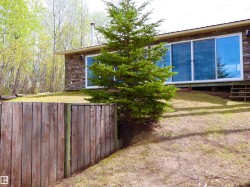 Stone veneer exterior with a prominent evergreen tree and a wooden fence - 