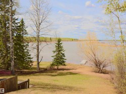 Waterfront property featuring a grassy bank, mature trees, a small wooden dock, and a distant shoreline - 
