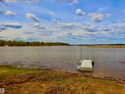 Waterfront property featuring a floating dock, natural shoreline, and distant tree line - 