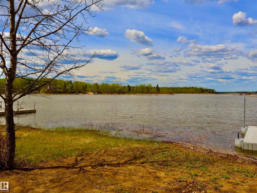 Expansive waterfront property featuring a tranquil lake, partial dock structures, and a verdant treeline across the water - #26 5508 Twp Rd 593A, Rural Barrhead County, AB - Outdoor With Body Of Water With View