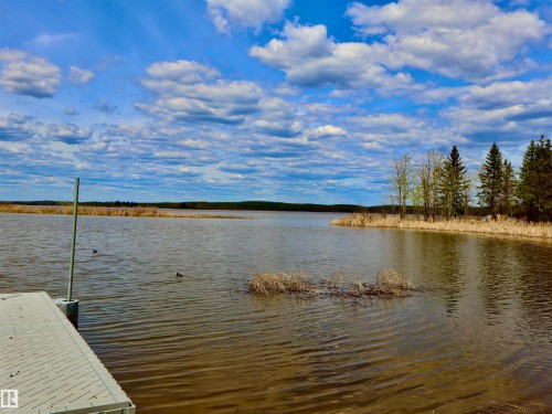 Waterfront property featuring a private dock, expansive water frontage, mature evergreen trees, and natural shoreline vegetation - #26 5508 Twp Rd 593A, Rural Barrhead County, AB - Outdoor With Body Of Water With View
