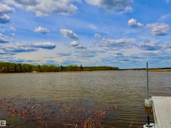 Waterfront property featuring a dock system, natural shoreline, and distant tree line - 