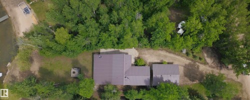 Property featuring a multi-building layout with metal roofs, surrounded by mature trees, and a shoreline with a dock structure - #26 5508 Twp Rd 593A, Rural Barrhead County, AB - Outdoor With View
