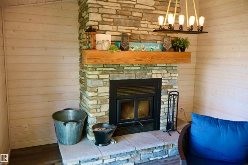 Stacked stone fireplace with a substantial timber mantelpiece and a built-in wood-burning insert - #26 5508 Twp Rd 593A, Rural Barrhead County, AB - Indoor With Fireplace