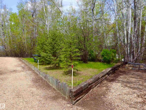 Landscaped gravel area featuring a wood retaining wall and mature trees - #26 5508 Twp Rd 593A, Rural Barrhead County, AB - Outdoor