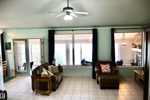 Spacious living area featuring light-toned tile flooring, multiple large windows, and a glass-paneled door - #26 5508 Twp Rd 593A, Rural Barrhead County, AB - Indoor