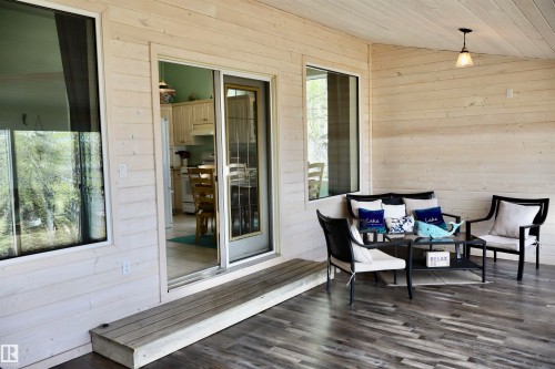 Covered outdoor patio featuring wood-finish flooring, paneled walls, a single-step entry, and a ceiling-mounted pendant light - #26 5508 Twp Rd 593A, Rural Barrhead County, AB - Outdoor With Deck Patio Veranda With Exterior