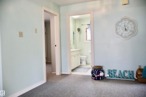 Light blue wall color and speckled carpeting, with a white trim doorway revealing a bathroom with a white vanity and toilet - #26 5508 Twp Rd 593A, Rural Barrhead County, AB - Indoor