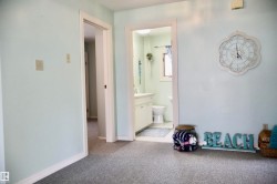 Light blue wall color and speckled carpeting, with a white trim doorway revealing a bathroom with a white vanity and toilet - 