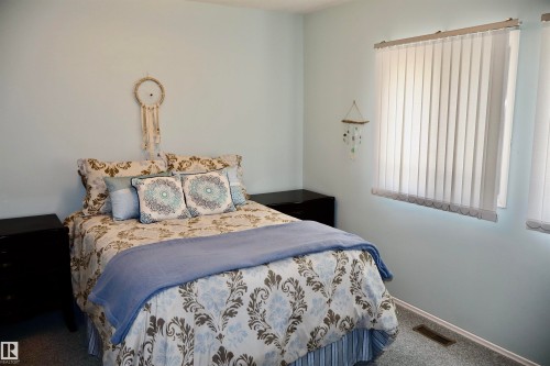 Bedroom featuring light blue walls, two windows with vertical blinds, and dark-toned bedside tables - #26 5508 Twp Rd 593A, Rural Barrhead County, AB - Indoor Photo Showing Bedroom