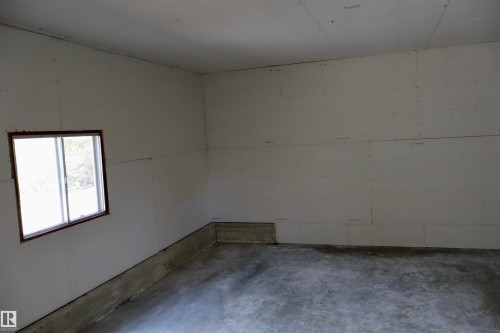 Interior space featuring unfinished drywall walls and ceiling, concrete flooring, and a single pane window with dark trim - #26 5508 Twp Rd 593A, Rural Barrhead County, AB - Indoor