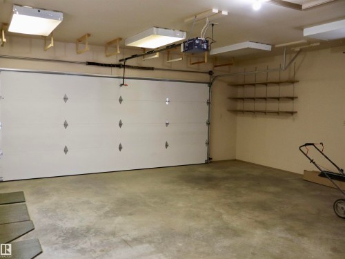 Spacious garage with a sectional overhead door, overhead fluorescent lighting, and built-in wall shelving - #26 5508 Twp Rd 593A, Rural Barrhead County, AB - Indoor Photo Showing Garage