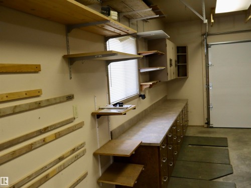 Garage workshop area featuring extensive built-in shelving, a large workbench with integrated storage drawers, upper cabinetry, and a window with blinds - #26 5508 Twp Rd 593A, Rural Barrhead County, AB - Indoor Photo Showing Other Room