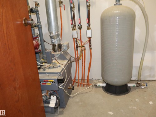 Utility area featuring a water heater, boiler system, exposed plumbing, and concrete flooring - #26 5508 Twp Rd 593A, Rural Barrhead County, AB - Indoor Photo Showing Basement