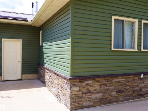 Exterior featuring green horizontal siding, stacked stone veneer detailing, and a concrete patio surface - #26 5508 Twp Rd 593A, Rural Barrhead County, AB - Outdoor With Exterior